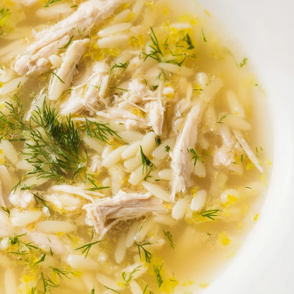 A steaming bowl of homemade Chicken Lemon Orzo Soup, featuring tender shredded chicken, bright lemon slices, and delicate orzo pasta swimming in a savory vegetable broth.