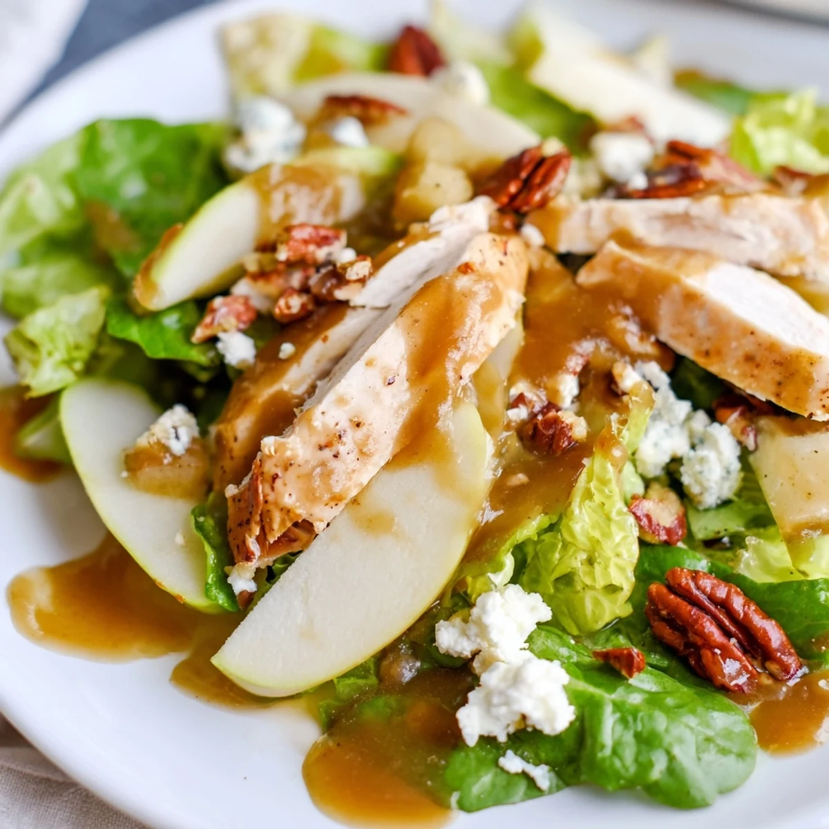 Freshly tossed Caramel Apple Chicken Salad with vibrant greens, juicy apple wedges, dried cranberries, and crumbled feta, drizzled with caramel-pecan dressing.