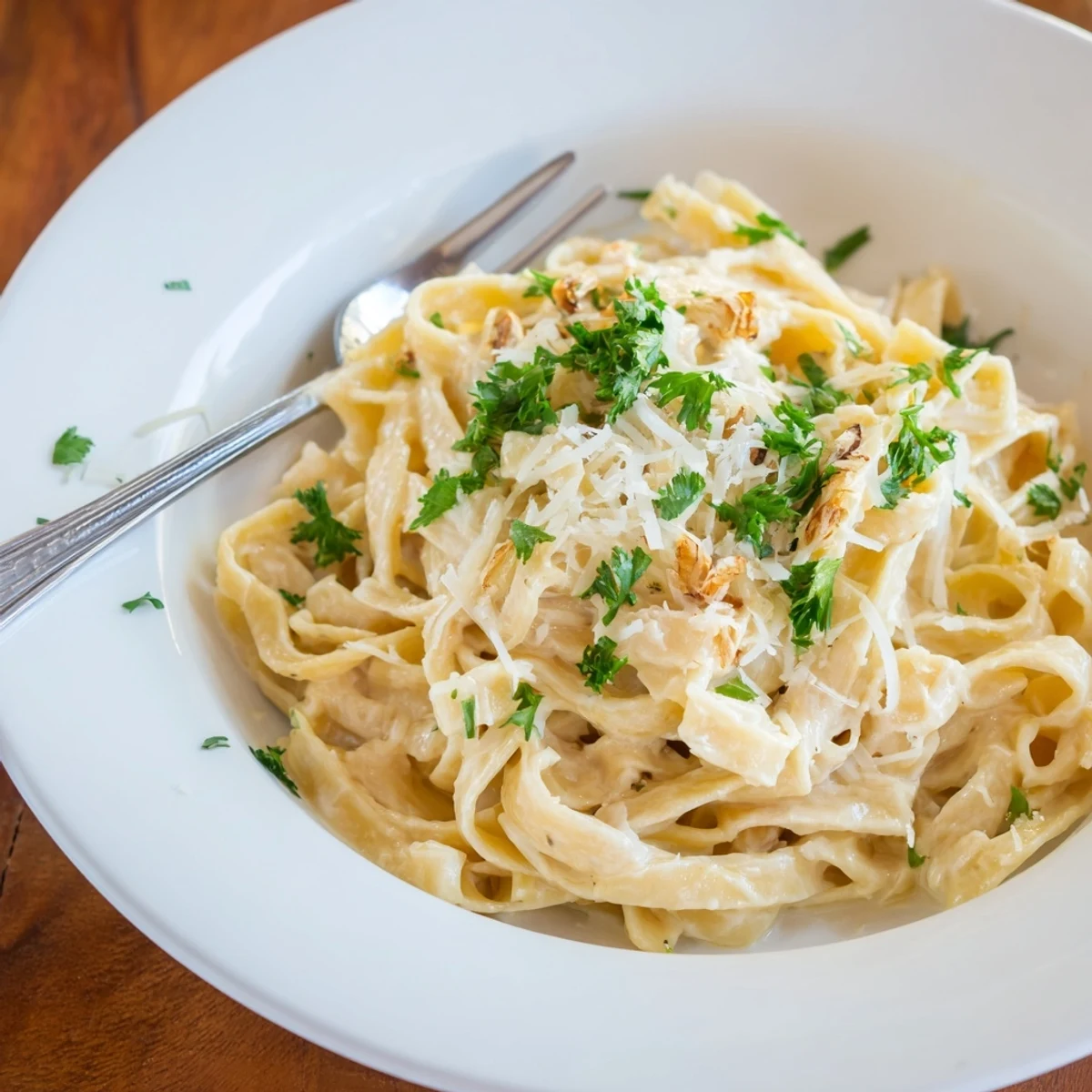 Serving suggestion of roasted garlic cream pasta on a white plate, topped with extra Parmesan.