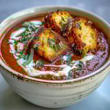 Creamy roasted tomato soup garnished with golden croutons and basil, served warm in a rustic white bowl.