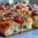 Vibrant herb focaccia with rosemary, thyme, and basil scattered over a crisp, golden crust, perfect for spring dining.  