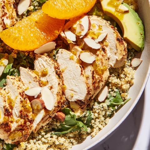 Grilled herb chicken slices rest on quinoa and greens, topped with orange segments, avocado, and red onion in a vibrant bowl.