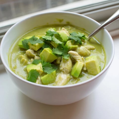 Tender shredded chicken simmered in a vibrant, tangy green salsa verde, served steaming in a rustic bowl with cilantro garnish.