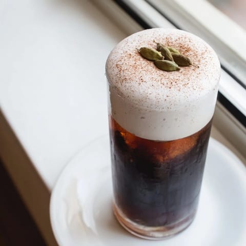 A close-up of a glass filled with homemade iced chai, boasting a thick, creamy cold foam topping.