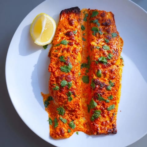 A close-up of flaky, perfectly cooked Indian Tikka Salmon, served with fresh coriander and lemon.