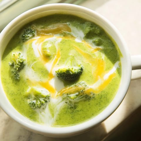 A warm mug of broccoli cheddar soup is served beside crusty artisan bread.