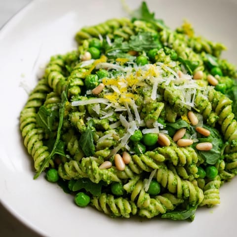 Spring Green Pesto Pasta Salad served chilled, mixed with fresh lemon zest, crunchy toasted pine nuts, and optional crumbled feta cheese.  