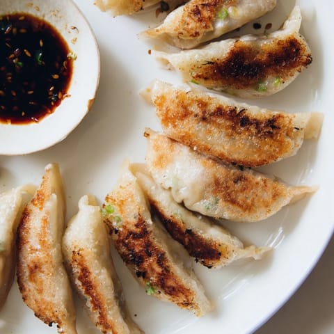 A close-up view of smashed gyozas on a plate, served with a small bowl of soy-vinegar dipping sauce and sesame seeds.