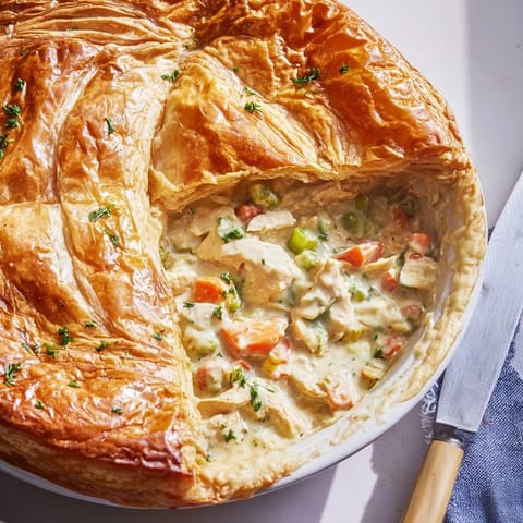 Freshly baked Chicken and Leek Pie with a golden crust rests on a rustic wooden board. 
