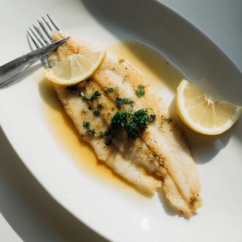 Flounder meunière fillets served on a white plate with lemon wedges and bright parsley garnish.