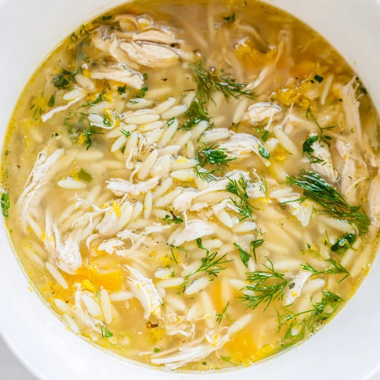 A close-up photo of vibrant Chicken Lemon Orzo Soup, highlighting fluffy orzo, diced carrots, and fresh dill garnish on a rustic kitchen table.
