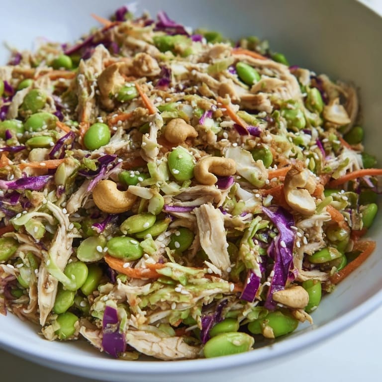 Close-up of Edamame Crunch Chicken Salad showing crunchy nuts, sesame seeds, and bright red bell peppers in a serving bowl.